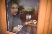 Nachdenkliche Frau bei einer Tasse Kaffee, während sie ihr Handy im Café benutzt — Stockfoto