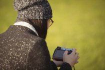 Visão traseira da mulher olhando para fotos na câmera digital em um dia ensolarado — Fotografia de Stock