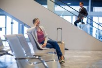 Mujer sonriente hablando por teléfono móvil en la sala de espera en la terminal del aeropuerto - foto de stock