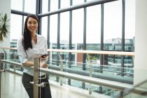 Portrait of smiling businesswoman holding mobile phone in office corridor — Stock Photo