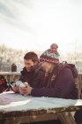 Счастливая пара лыжников с помощью мобильного телефона и цифрового планшета за столом в горнолыжном курорте — стоковое фото