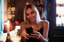 Красива усміхнена жінка використовує мобільний телефон в барі — стокове фото