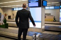 Вид ззаду бізнесмена, що стоїть з багажем в зоні очікування в аеропорту — стокове фото
