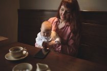 Мати тримає милий немовля в руках за журнальним столиком — стокове фото