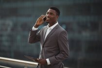 Бизнесмен, держащий цифровой планшет и разговаривающий по мобильному телефону на офисной террасе — стоковое фото