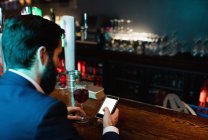 Empresário usando telefone celular enquanto toma um copo de vinho no balcão do bar — Fotografia de Stock
