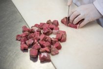 Gros plan du boucher coupant la viande en petits morceaux à l'usine de viande — Photo de stock