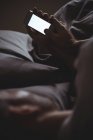 Чоловік використовує свій мобільний телефон, розслабляючись на ліжку вдома — стокове фото