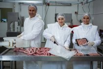 Женщины и мужчины-мясники упаковывают колбасы на мясокомбинате — стоковое фото