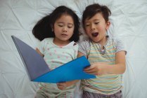 Братья и сестры лежат и читают книги в спальне дома — стоковое фото