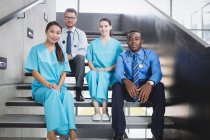 Portrait of smiling doctors and nurses sitting on staircase in hospital — Stock Photo