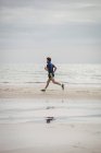 Athlete running along beach with wet sand — Stock Photo