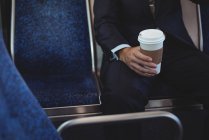 Mid section of businessman holding a disposable coffee cup while travelling in bus — Stock Photo