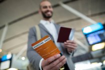 Homme d'affaires souriant montrant sa carte d'embarquement au terminal de l'aéroport — Photo de stock