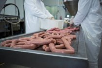 Corte médio de açougueiros que processam salsichas em fábrica de carne — Fotografia de Stock