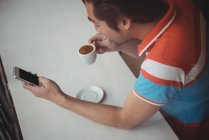 Високий кут зору чоловіка, який використовує мобільний телефон, маючи каву в кав'ярні — стокове фото