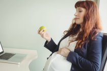Embarazada mujer de negocios sosteniendo manzana en el cargo - foto de stock