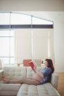 Pregnant woman reading book on sofa in living room at home — Stock Photo