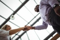 Vista de bajo ángulo de los ejecutivos de negocios estrechando la mano en el pasillo de la oficina - foto de stock