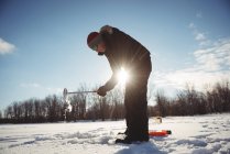 Ice fisherman digging hole in snowy landscape — Stock Photo