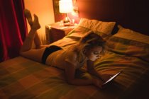 Женщина лежит и использует цифровой планшет на кровати в спальне — стоковое фото