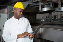 Serious male worker wearing lab coat while using laptop in juice factory — Stock Photo