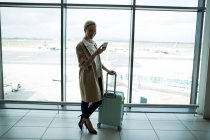 Бизнесвумен с багажом с помощью мобильного телефона в аэропорту — стоковое фото