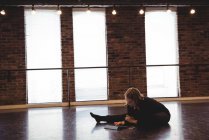 Танцівниця сидить на підлозі, розтягується і використовує цифровий планшет у танцювальній студії — стокове фото