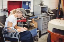 Scrittura meccanica femminile su notebook in garage di riparazione — Foto stock