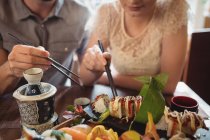 Sección media de la pareja tomando sushi en el restaurante - foto de stock
