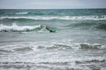Homem de terno molhado nadando no mar na praia — Fotografia de Stock
