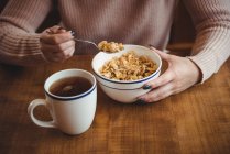Mujer tomando cereales en tazón para desayunar en casa - foto de stock