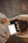 Vista de alto ângulo da mulher com tablet digital tomando café da manhã em casa — Fotografia de Stock