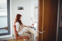 Беременная женщина с ноутбуком в кабинете дома — стоковое фото