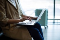 Средняя секция деловой женщины, использующей ноутбук в аэропорту — стоковое фото