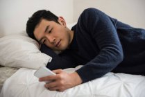 Человек, использующий мобильный телефон на кровати дома — стоковое фото