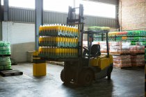 Pila de botellas de jugo envasadas y montacargas en almacén de distribución - foto de stock