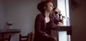 Mujer pensativa tomando una taza de café en la cafetería - foto de stock