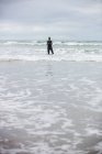 Atleta in muta in piedi con le mani incrociate in mare sulla spiaggia — Foto stock