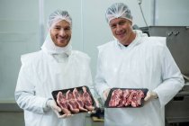 Portrait of butchers holding meat trays at meat factory — Stock Photo