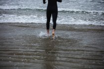 Baixa seção de atleta em terno molhado caminhando em direção ao mar — Fotografia de Stock