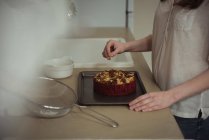 Sección media de la mujer que cuece la torta horneada en la cocina en casa - foto de stock