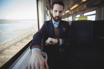 Homme d'affaires vérifiant le temps sur smartwatch tout en voyageant en train — Photo de stock