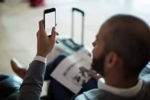 Empresario que usa teléfono móvil en la sala de espera en la terminal del aeropuerto - foto de stock