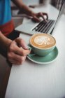 Середина людини використовує ноутбук і тримає чашку кави в кав'ярні — стокове фото
