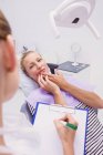 Doctor writing  report of female patient with toothache in clinic — Stock Photo