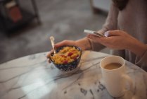 Крупный план женщины, использующей мобильный телефон во время завтрака дома — стоковое фото