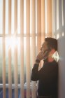 Чоловік-виконавчий виступ на мобільному телефоні біля віконних жалюзі в офісі — стокове фото