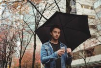 Чоловік використовує мобільний телефон і тримає парасольку на вулиці — стокове фото