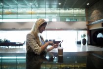 Smiling woman using mobile phone in waiting area at airport terminal — Stock Photo